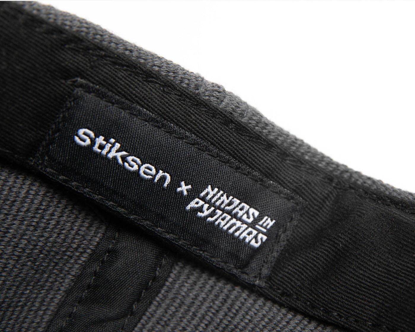 A black ninja cap from the NIP X Stiksen merch collaboration, featuring the Ninjas in Pyjamas logo subtly embroidered on the front. This stylish and adjustable cap is perfect for showcasing your support for NIP in a sleek and trendy way.
